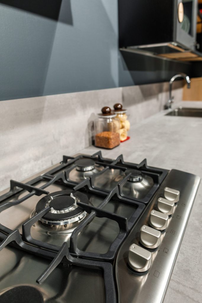 A stainless gas cooktop seen close along its cast-iron grates, the knobs down the right side, dark surround