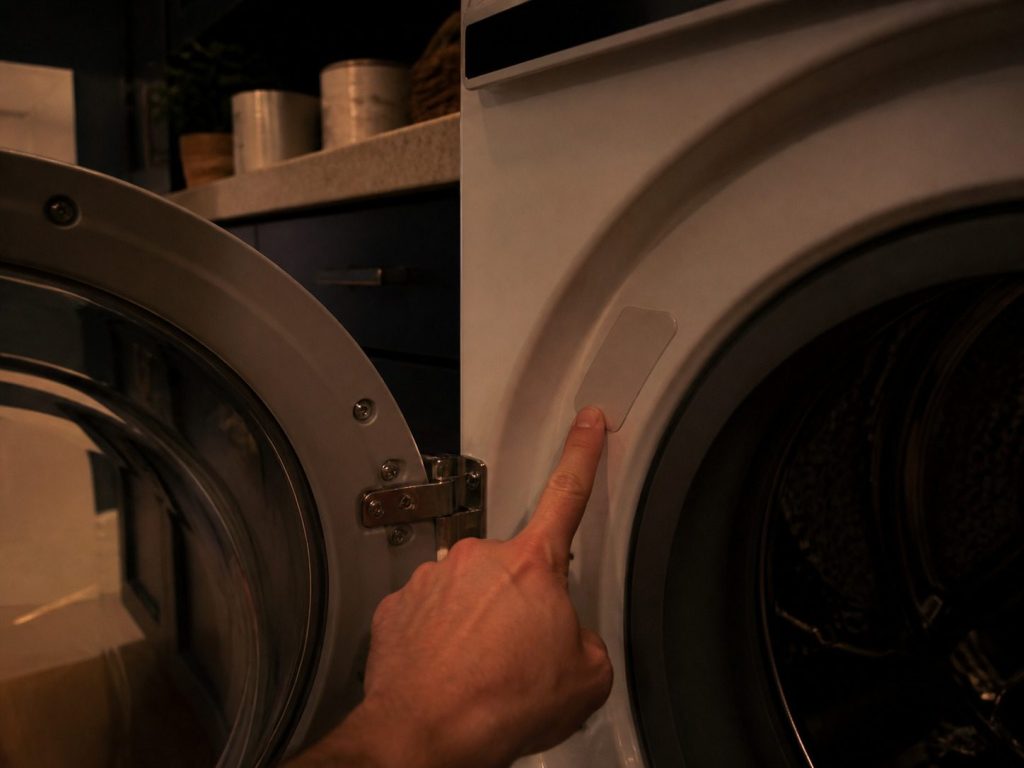 An appliance door swung wide with the plate on the jamb behind it and a fingertip on it.