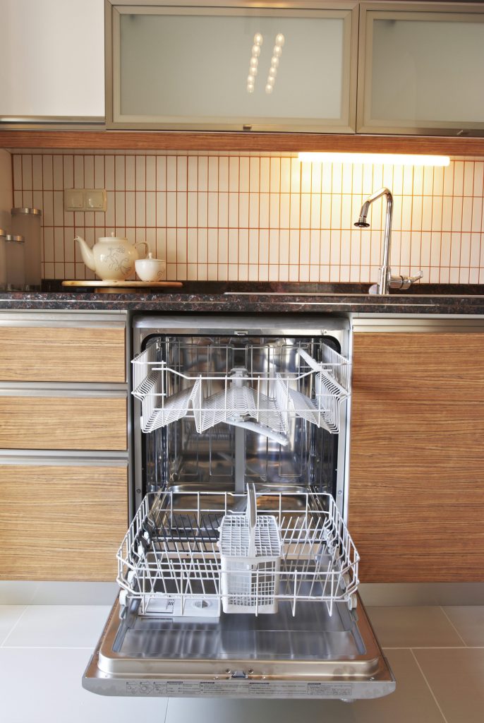 A built-in dishwasher seen low from floor level along the toe kick, door down and the lower rack drawn out into the room