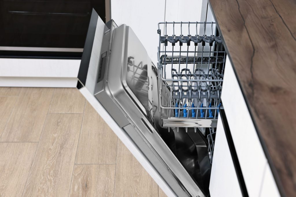 A built-in undercounter dishwasher seen from a high angle down across its open door, the upper rack drawn out and the tub empty