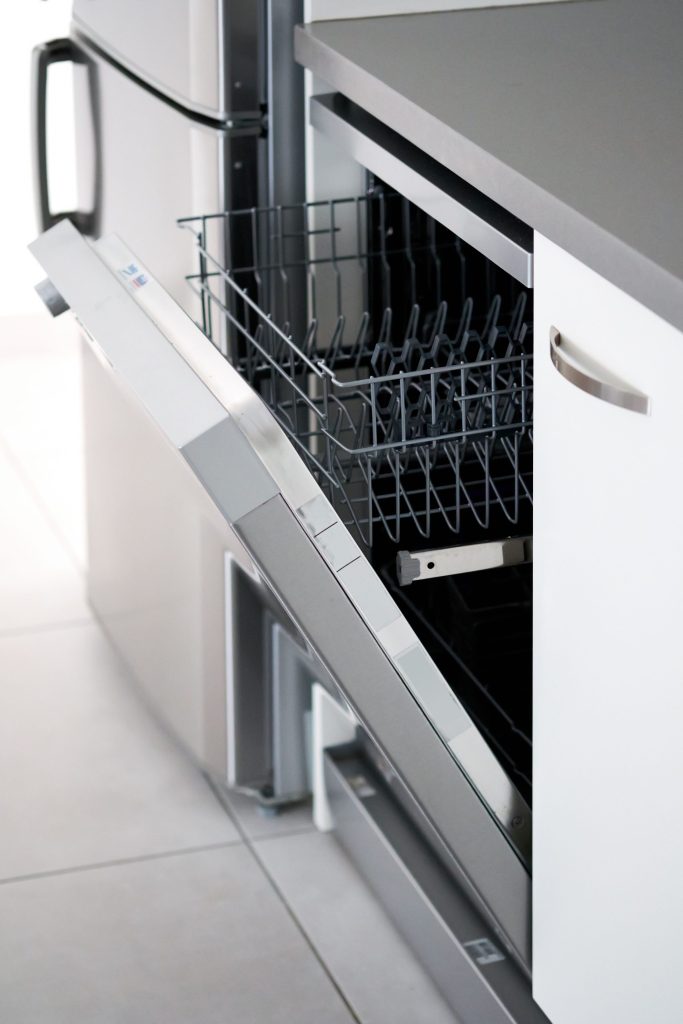 A tight three-quarter view of a stainless dishwasher door and its bar handle, the door part open on the upper rack
